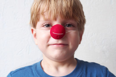 Close-up portrait of boy wearing clown nose against wall