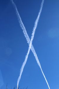 Low angle view of vapor trails against blue sky