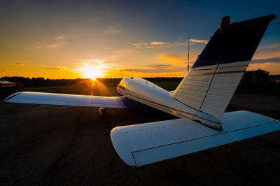 Airplane on airport runway against sky during sunset