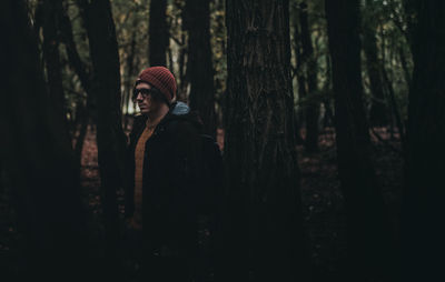 Man standing by tree trunk in forest