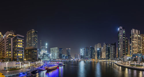 Illuminated buildings by river against sky at night