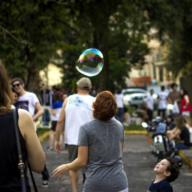 leisure activity, lifestyles, focus on foreground, childhood, togetherness, boys, casual clothing, girls, large group of people, enjoyment, fun, person, elementary age, rear view, day, bubble, tree, park - man made space