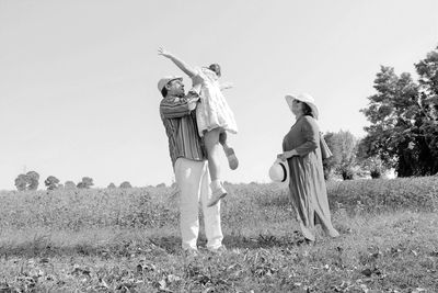 Mother looking at father carrying daughter while standing on field against clear sky