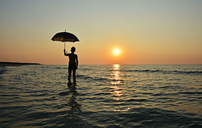 Silhouette people standing in sea against sunset sky