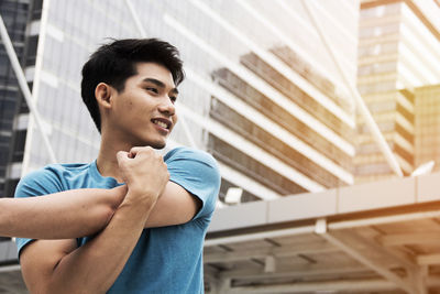 Smiling young man exercising against building