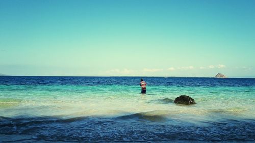 Rear view of man standing on beach against clear blue sky