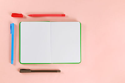 Directly above shot of diary and pens on pink background