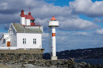 Lighthouse by buildings against sky