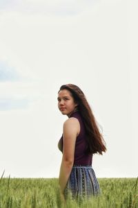 Young woman standing on field against sky