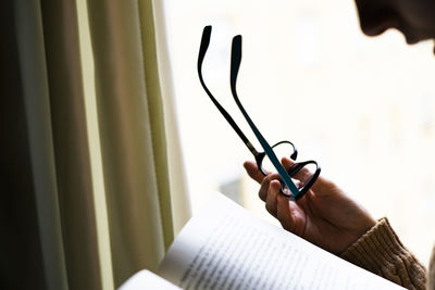 Woman reading a book with her reading glasses in her hand.