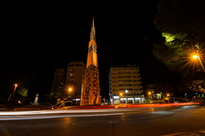 Illuminated light trails on city street by buildings at night