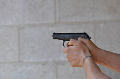 Close-up of man holding gun against wall