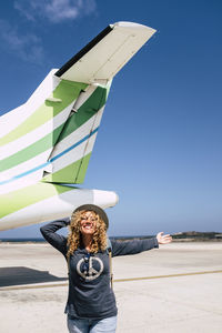 Woman standing at airport against airplane and sky