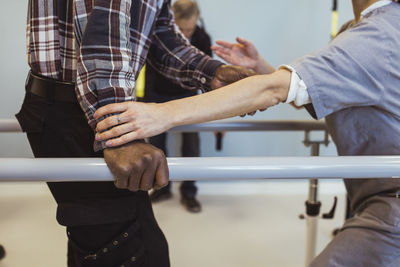 Midsection of female caregiver helping senior man to walk at retirement home