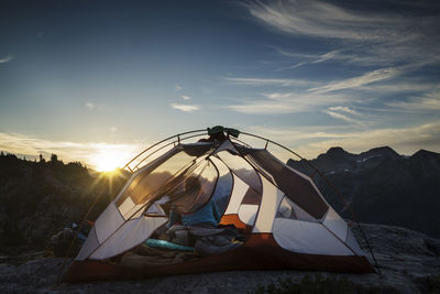 Rear view of woman sitting in tent against mountains during sunset