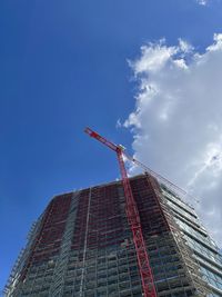 Low angle view of crane by building against sky