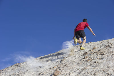 Low angle view of man jogging on mountain against clear blue sky