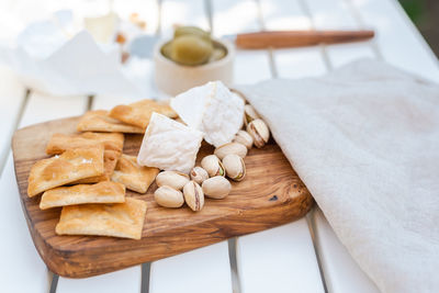 Wine appetizers namely pistachios, camembert cheese, saltine crackers and olives on table outdoors.