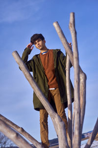 Young man looking away while standing by wooden posts against sky