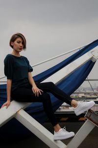 Full length portrait of young woman sitting on metal