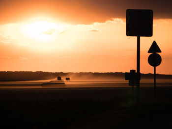 Silhouette road sign on field against sky during sunset