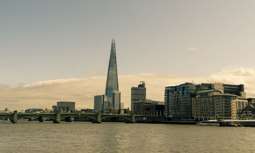 Modern buildings by river against sky in city