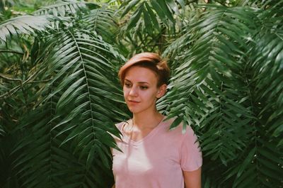 Portrait of young woman standing by palm tree