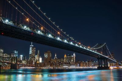 Manhattan bridge over east river against sky in illuminated city at night