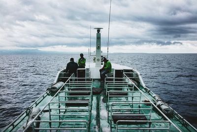 People on trawler in sea against cloudy sky