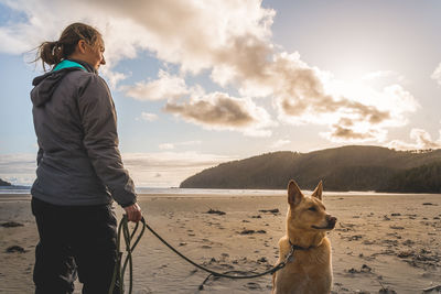 Woman with dog standing on shore at beach against sky