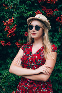 Beautiful young woman wearing sunglasses against red and plants