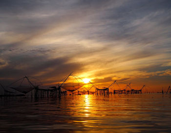 Silhouette fishing net by sea against sky during sunset