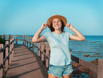 Smiling teen girl standing on wooden walkway by the sea at sunset