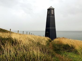 Lighthouse by sea against sky