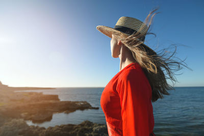 Portrait of a caucasian young woman in a red dress and straw hat on the seashore.  