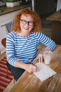 Portrait of smiling senior woman with sudoku while sitting at table