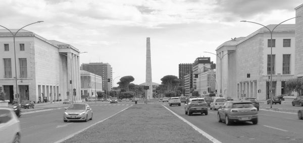 Traffic on road amidst buildings in city against sky