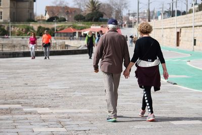 Rear view of people walking on sidewalk in city