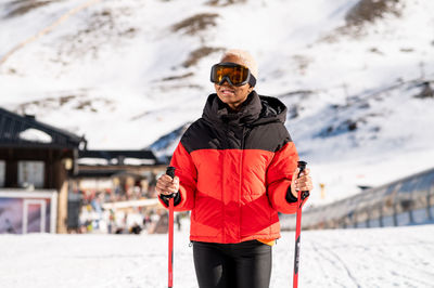 Una mujer afroamericana con bastones de esquí de pie en una montaña nevada durante el invierno