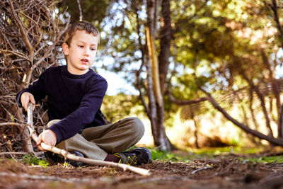 Surface level shot of boy holding stick sitting on ground