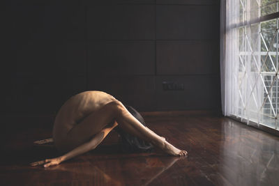 Side view of shirtless woman exercising on hardwood floor