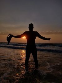 Silhouette man standing on beach against sky during sunset
