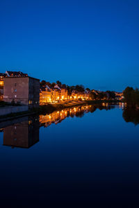 Reflection of illuminated buildings in lake against clear blue sky