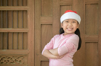 Portrait of smiling girl with arms crossed standing against door