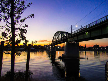 Silhouette bridge over river against sky at sunset