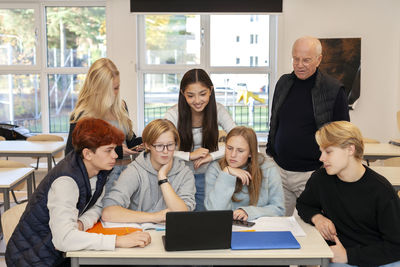 Teenage kids and teacher using laptop in classroom