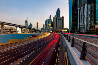 Light trails on road amidst buildings in city against sky