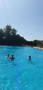 People swimming in pool against blue sky