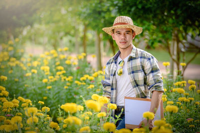 Portrait of man holding yellow flowers in field