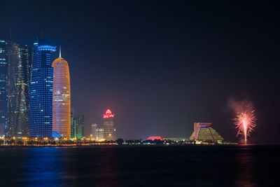 Illuminated city by river against sky at night